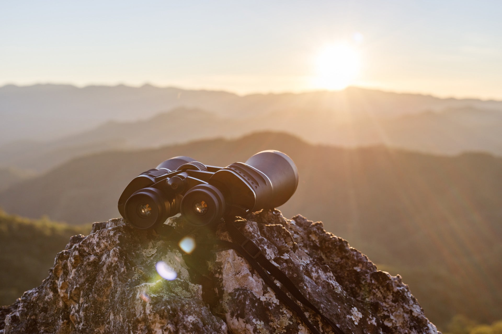 A photo of binoculars resting on a rock and pointed toward a sunrise over the hills. It represents AI futures worth building.